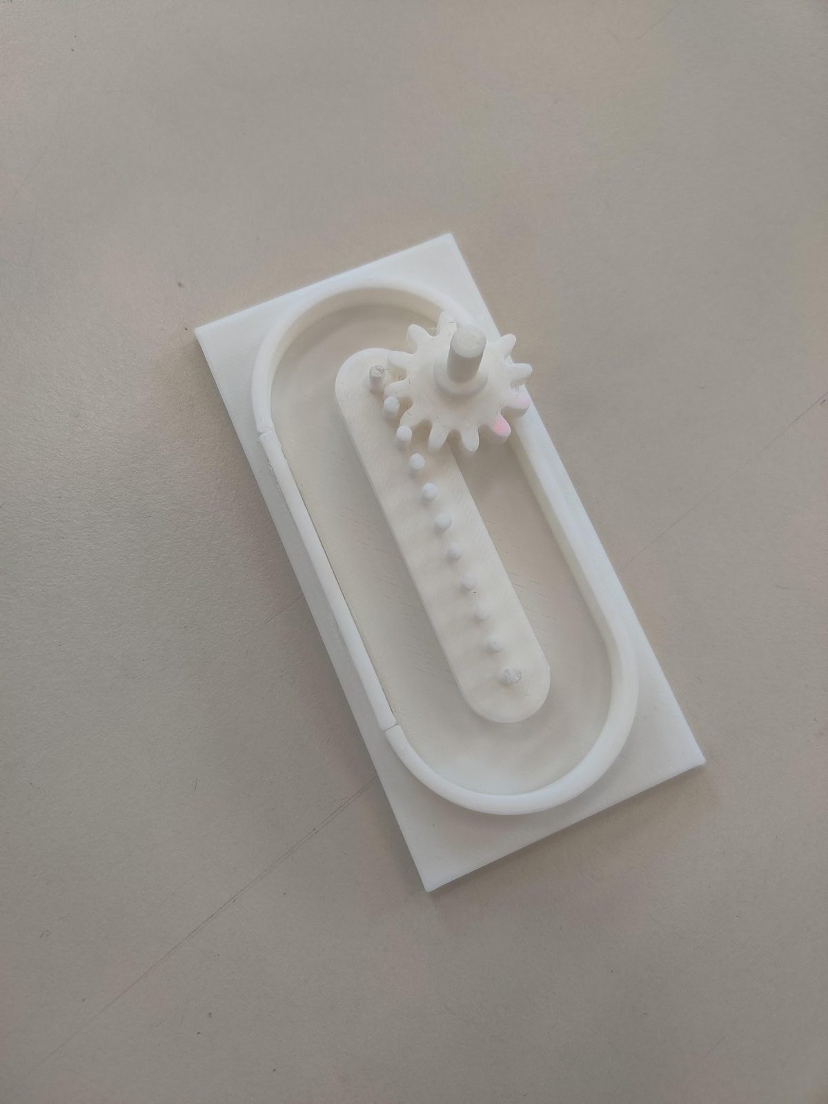 A finished 3D-printed mangle rack: a gear on a peg rack inside an oval track, all printed in white PLA