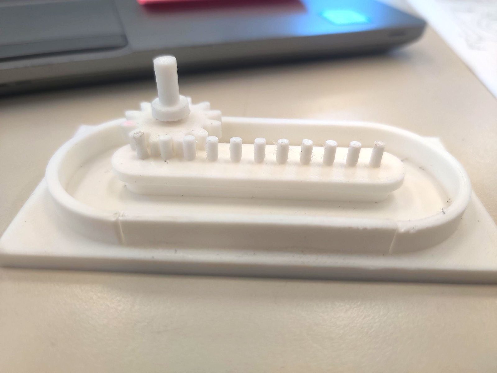 The first printed prototype: the gear on its axle beside a row of standing pegs inside the oval track