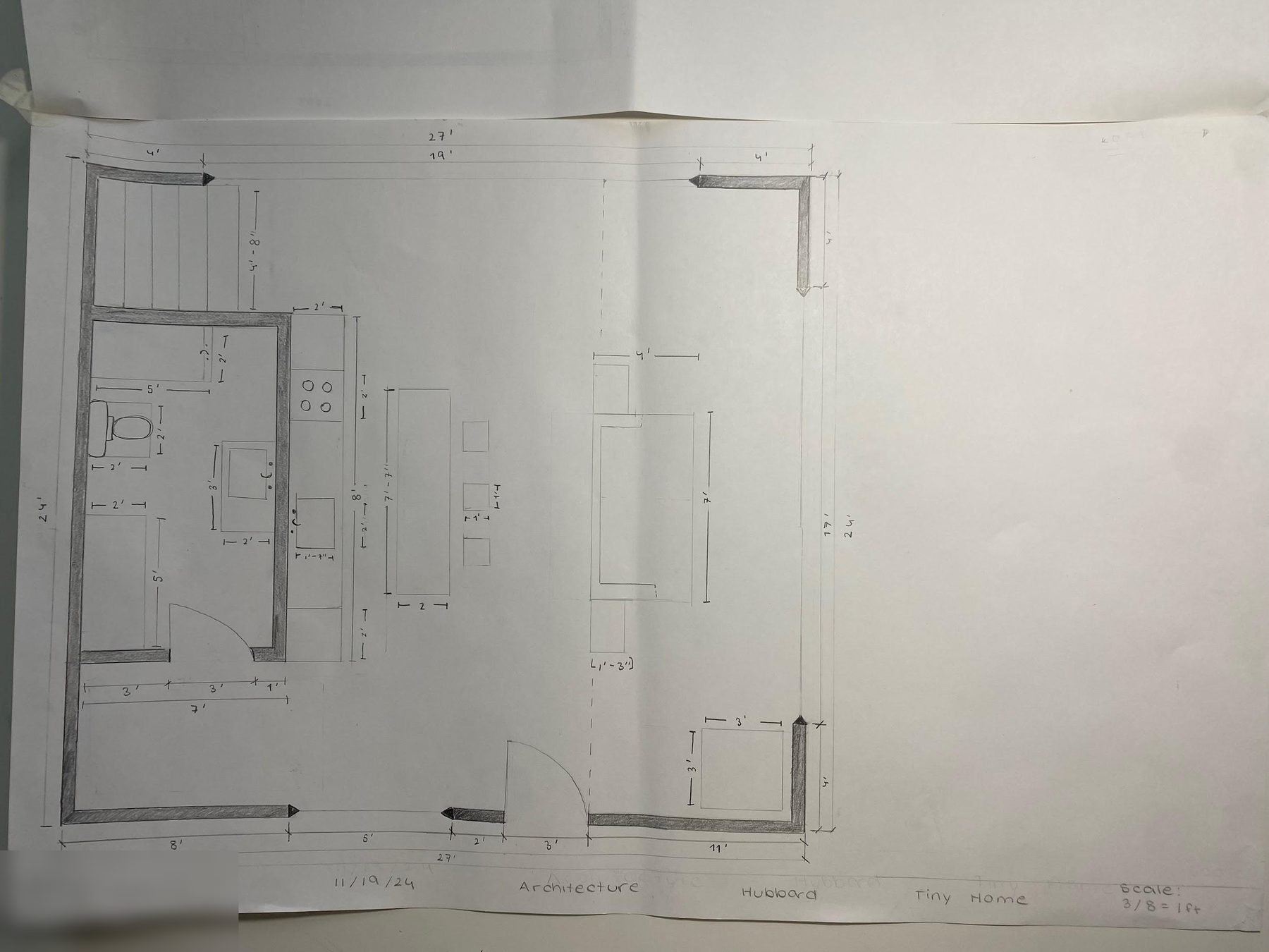A student tiny house floor plan, 24 by 27 feet, with dark walls, a bathroom, kitchen, island, stairs and dimension strings around the outside