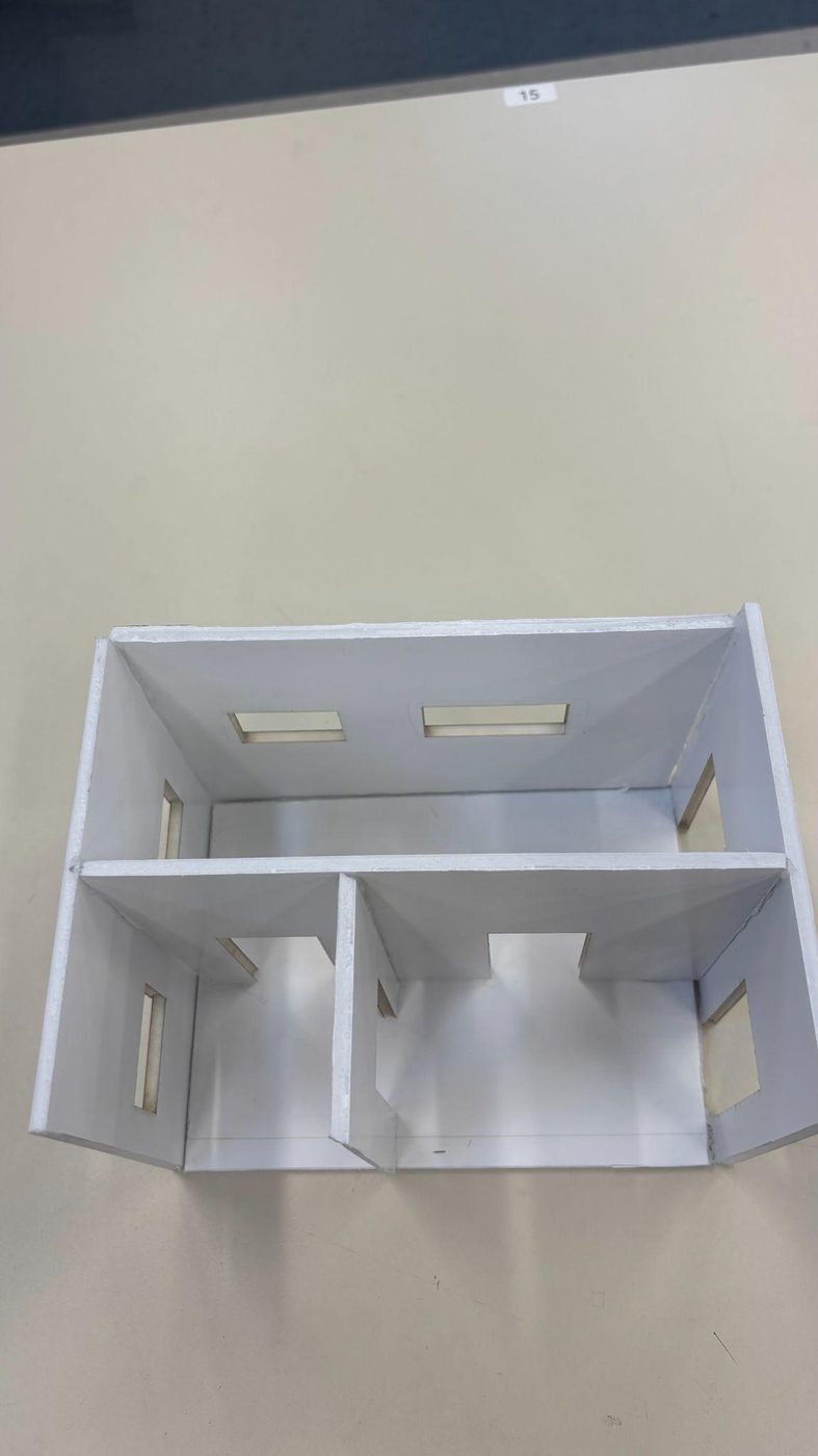 A foam board tiny house model seen from above with no roof, showing interior walls and window openings