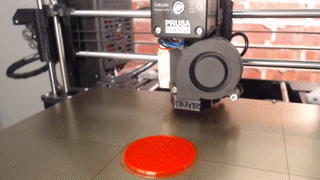 A red cube printing tilted on its corner, starting from a small circle on the bed